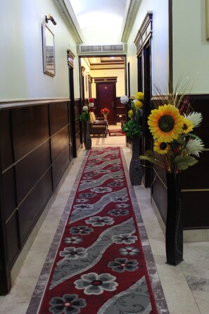 A hallway with a red floral carpet, dark walls, and a large vase with sunflowers. - City View Hotel (Cairo)