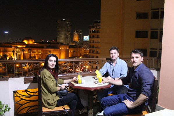 Three people seated at an outdoor table with drinks, overlooking a cityscape with illuminated buildings and a dome structure. - City View Hotel (Cairo)