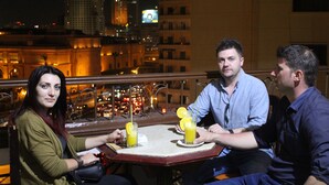 Three people seated at a table with drinks, overlooking a cityscape at night. - City View Hotel (Cairo)