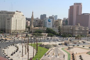 A cityscape with modern buildings, a prominent clock tower, and a large hotel with a visible logo. - City View Hotel (Cairo)