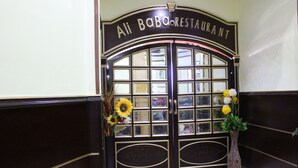 A black double door with glass panels and the sign "Ali Baba Restaurant" above it. There are two vases with flowers on either side of the door. - City View Hotel (Cairo)