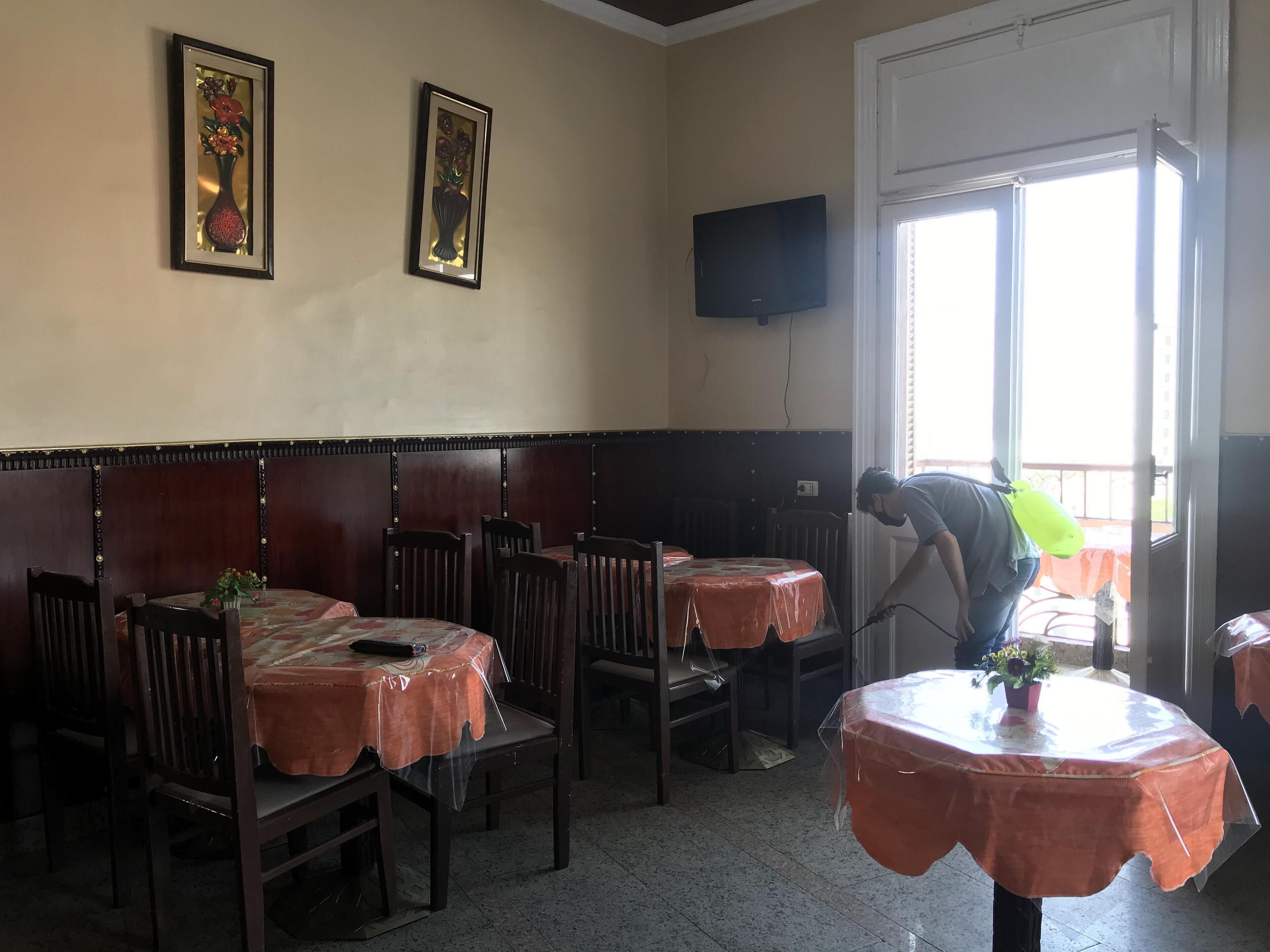 A dining area with tables covered in orange tablecloths, wooden chairs, and two framed floral artworks on the wall.