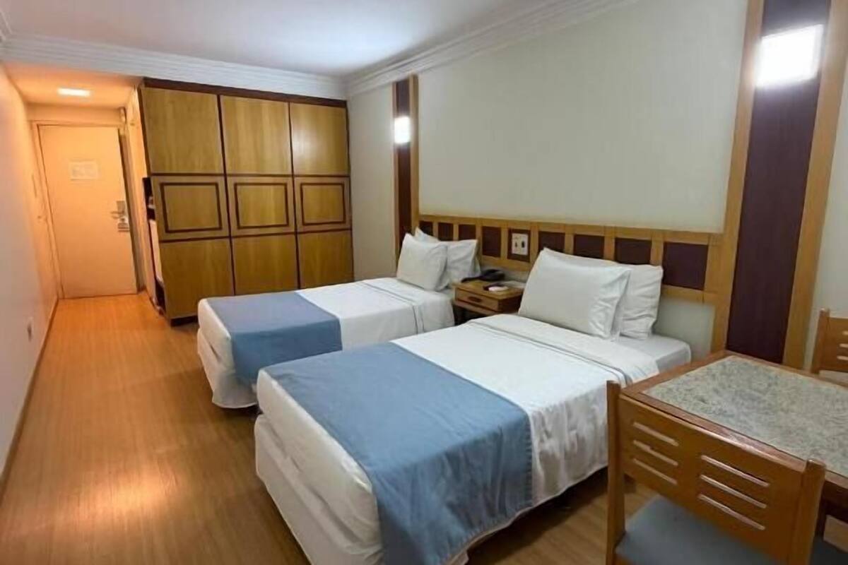 A small, compact room with two single beds, a wooden table, and a wardrobe.