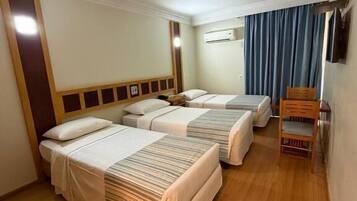 Quarto de hotel com três camas, uma cadeira de madeira e um aparelho de ar condicionado.