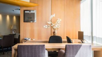 A hotel reception desk with a wooden panel wall, a vase of white flowers, a telephone, and a computer monitor.