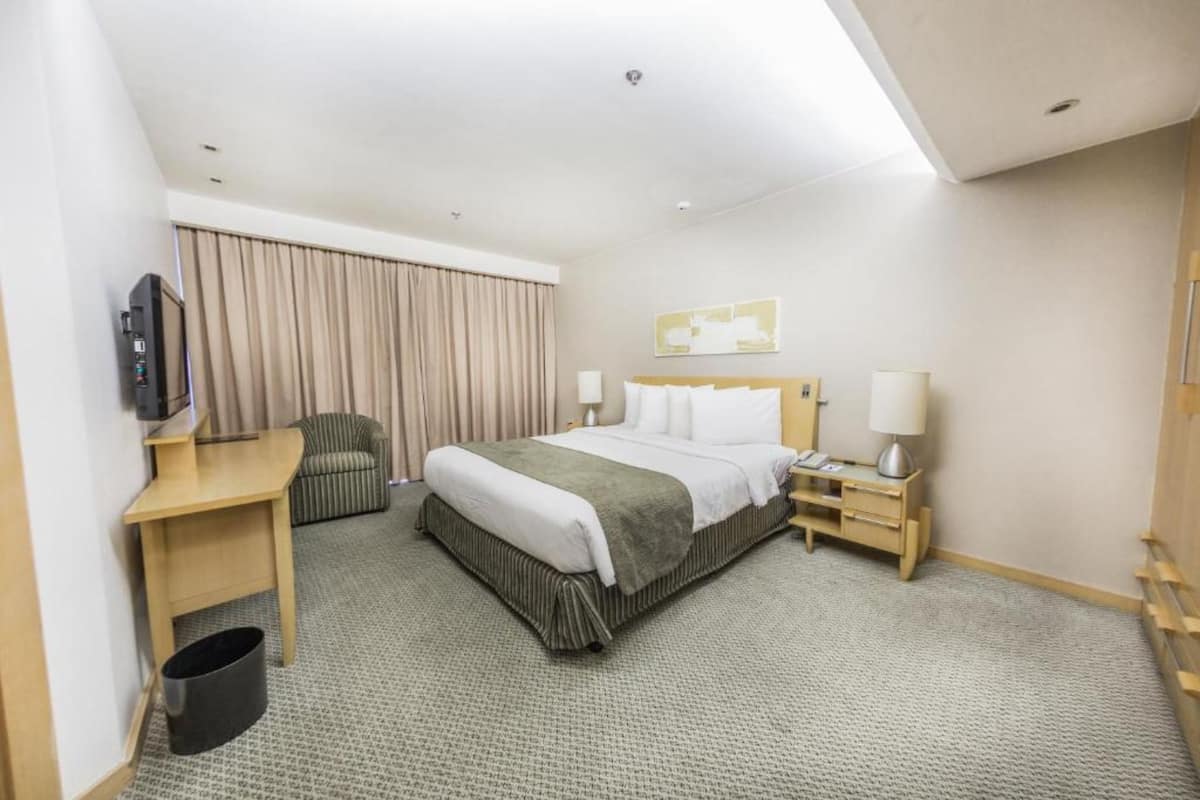 Una habitación de hotel con cama, escritorio, silla, televisor, lámpara y cubo de basura.