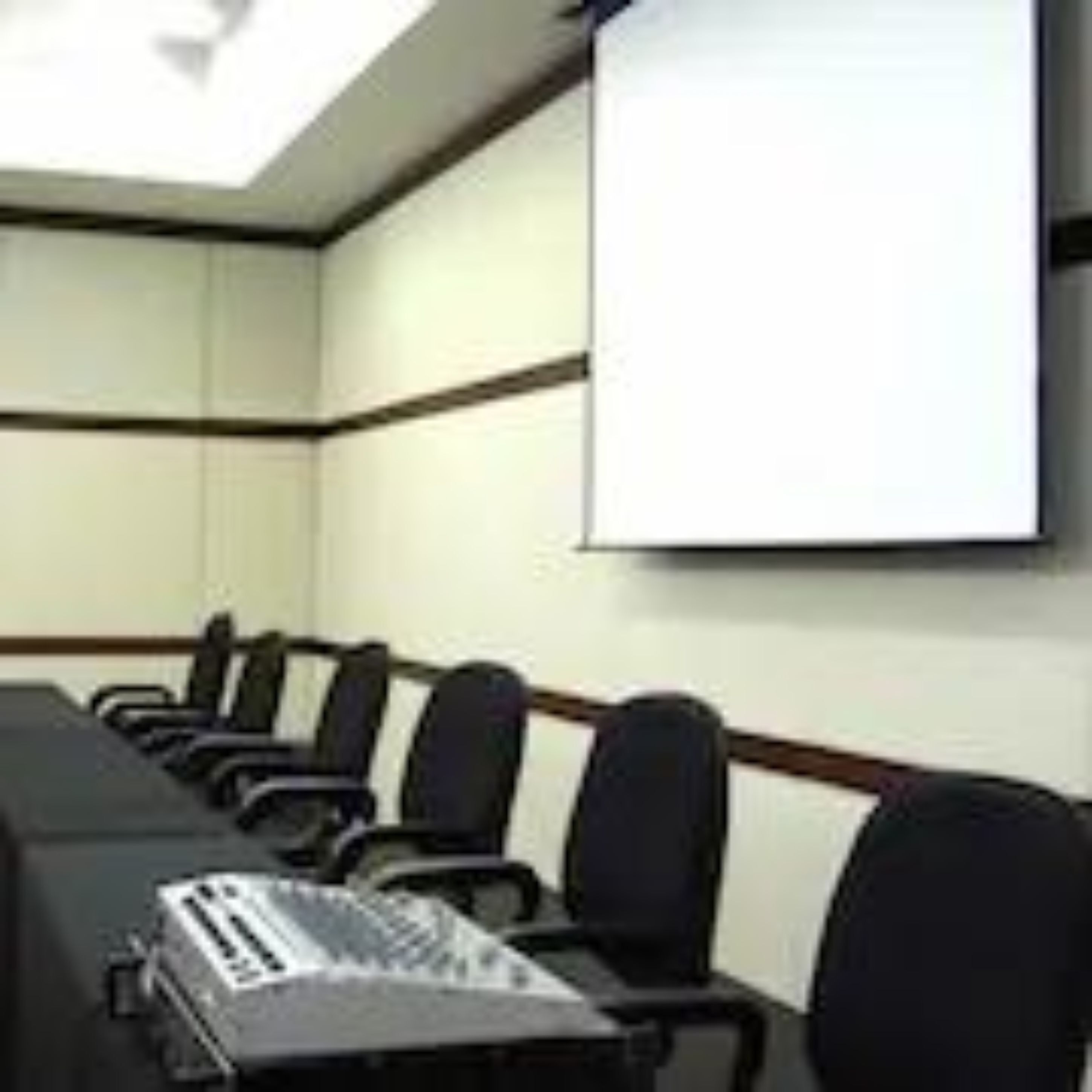 A conference room with a long table, several chairs, a projector screen, and a laptop.