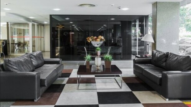Un hall d’entrée moderne avec deux canapés en cuir noir, une table basse centrale agrémentée d’un vase et de plantes, et un sol à carreaux.