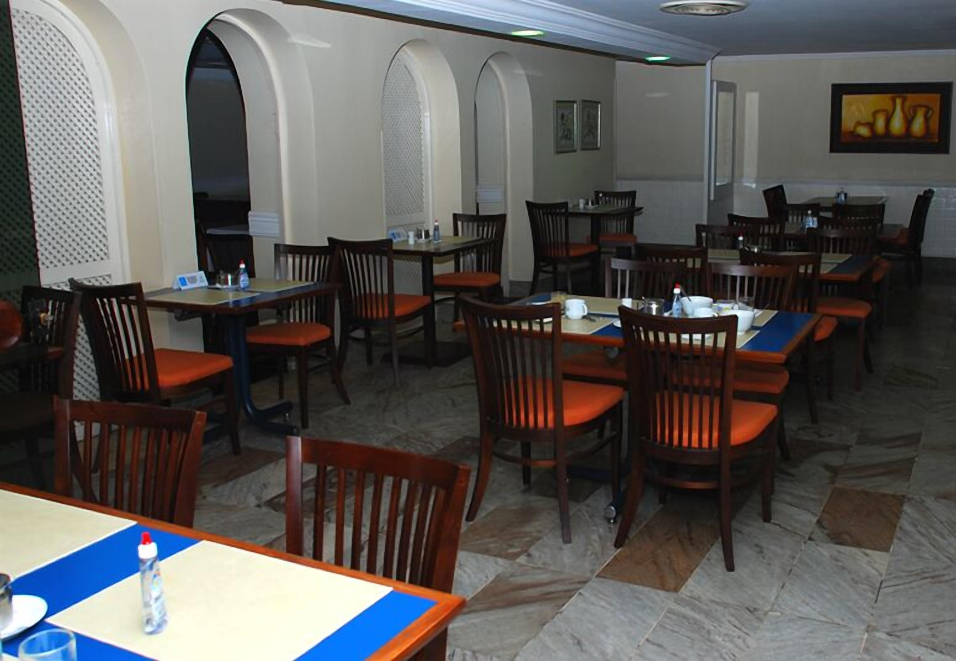 A restaurant with multiple tables and chairs, featuring a tiled floor and arched doorways.