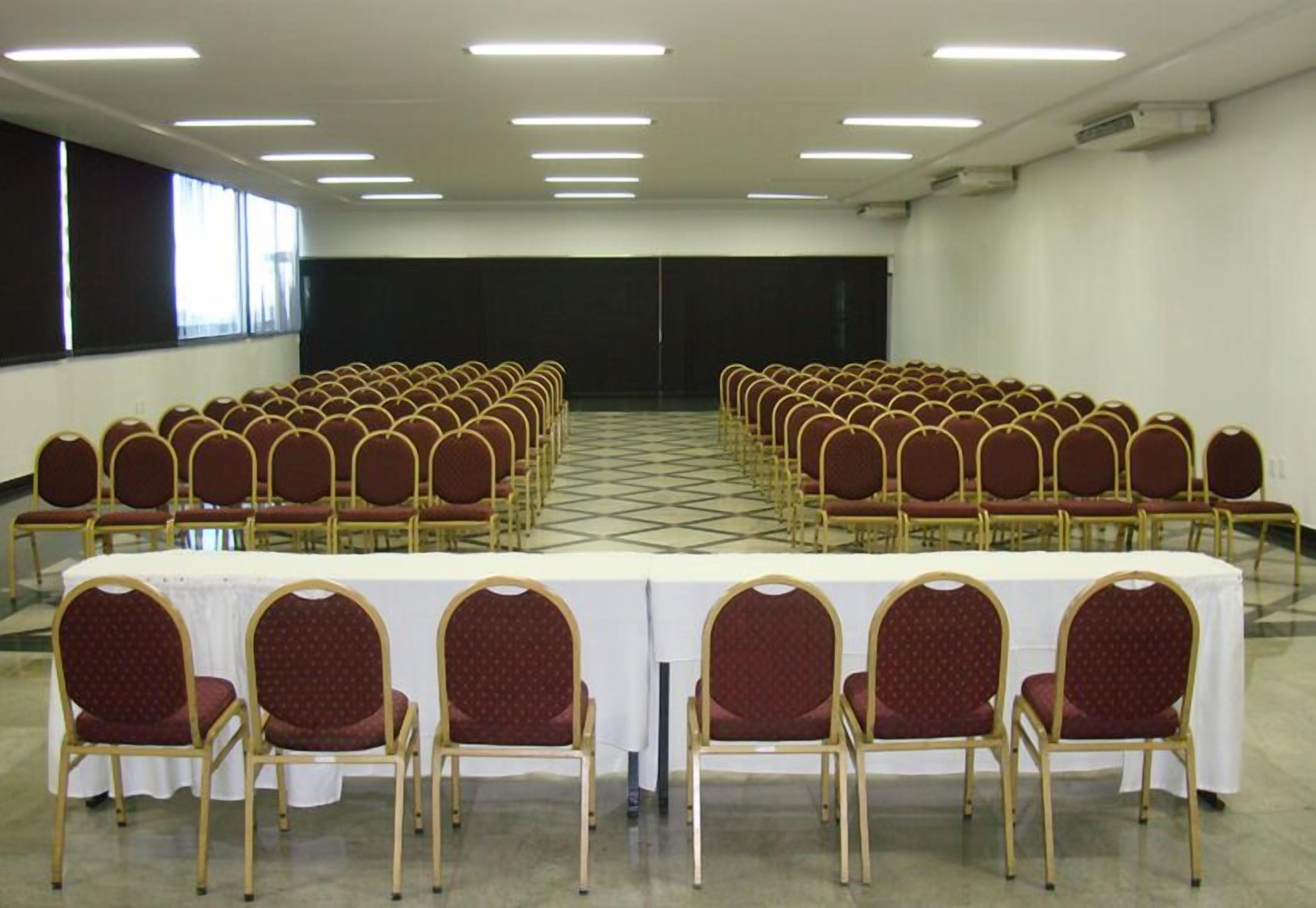 A conference room with rows of chairs and a long table, equipped with overhead lighting.