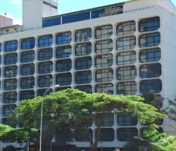 A multi-story building with a grid of windows and a tree in the foreground. - Phenícia Bittar Hotel (Brasília)