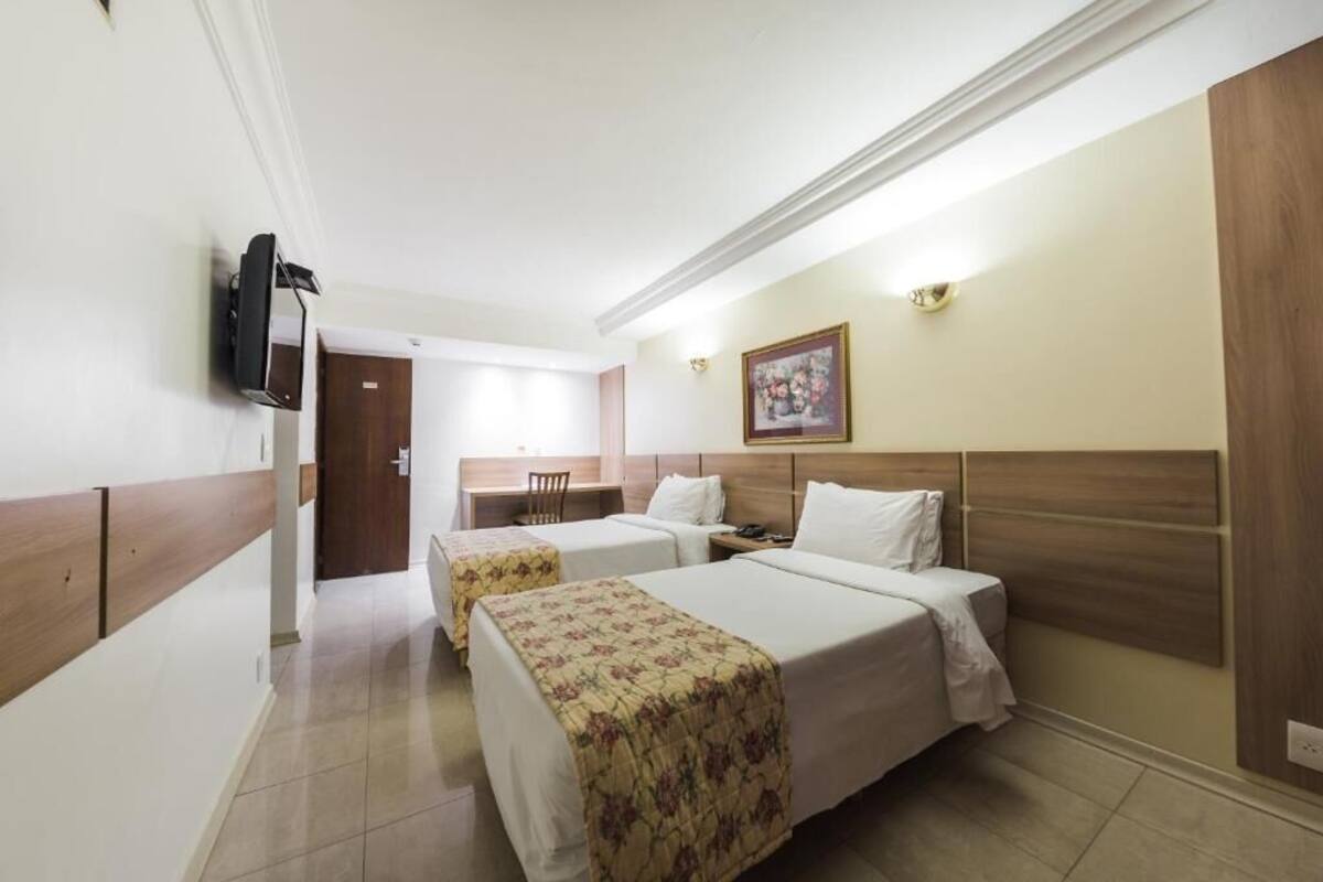 Une chambre d’hôtel avec deux lits, un bureau, une chaise, une télévision et un tableau au mur.