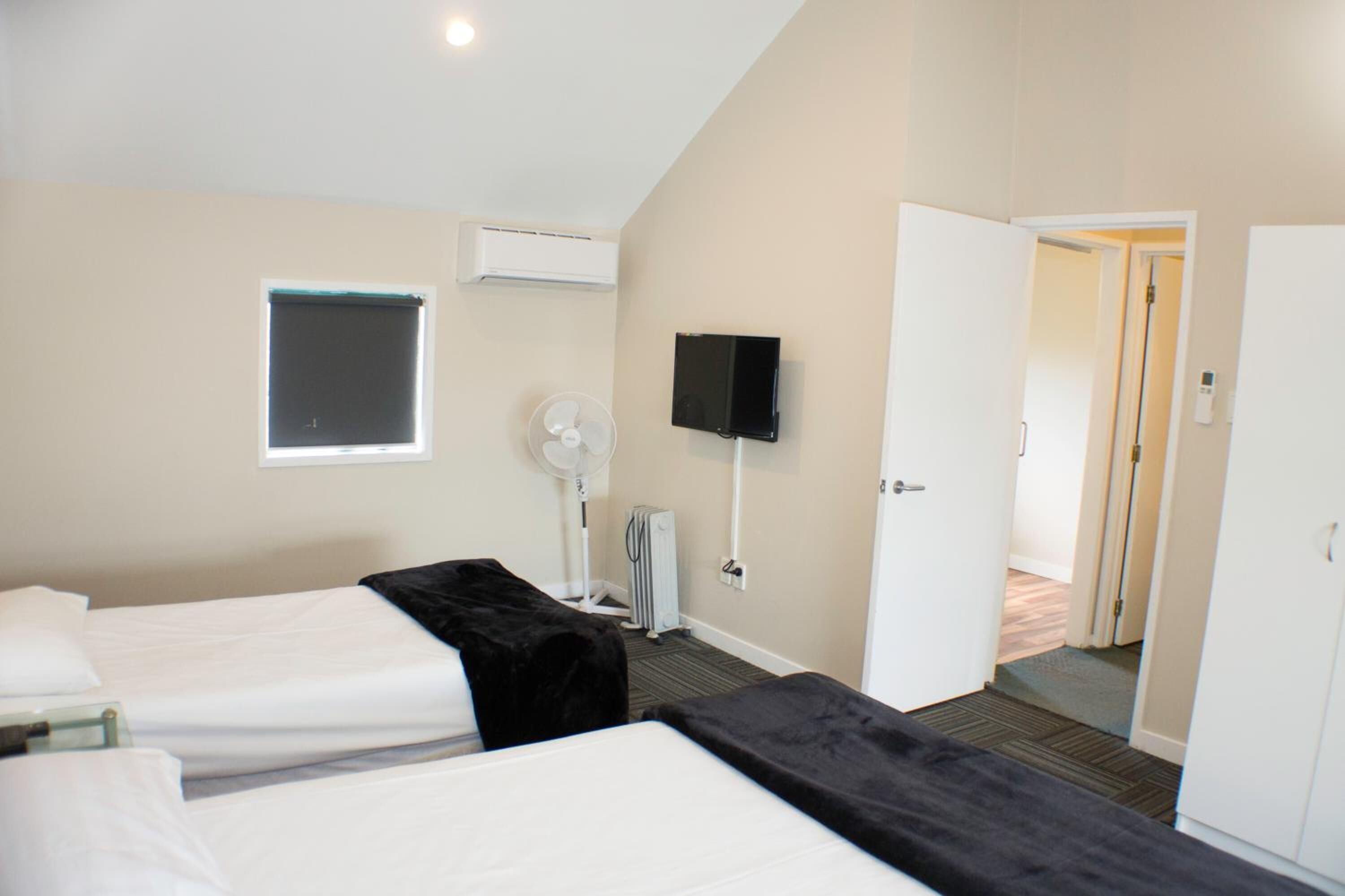 A hotel room with two beds, a flat-screen TV, a window, and an air conditioning unit.