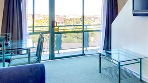 Una habitación con una mesa de vidrio, una silla, un sofá y un televisor en la pared.
