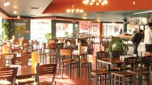 Un restaurante con varias mesas y sillas, una zona de bar y vistas a la calle.