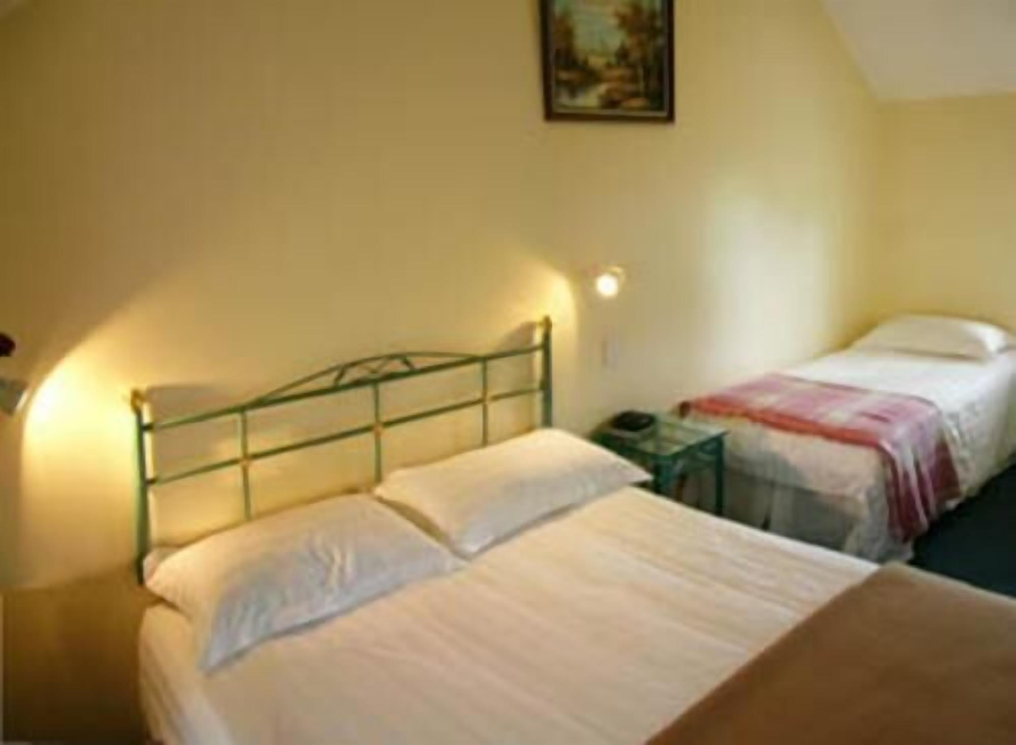 A room with two beds, a nightstand, and a wall-mounted lamp.