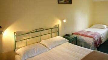 A room with two beds, a nightstand, and a wall-mounted lamp.