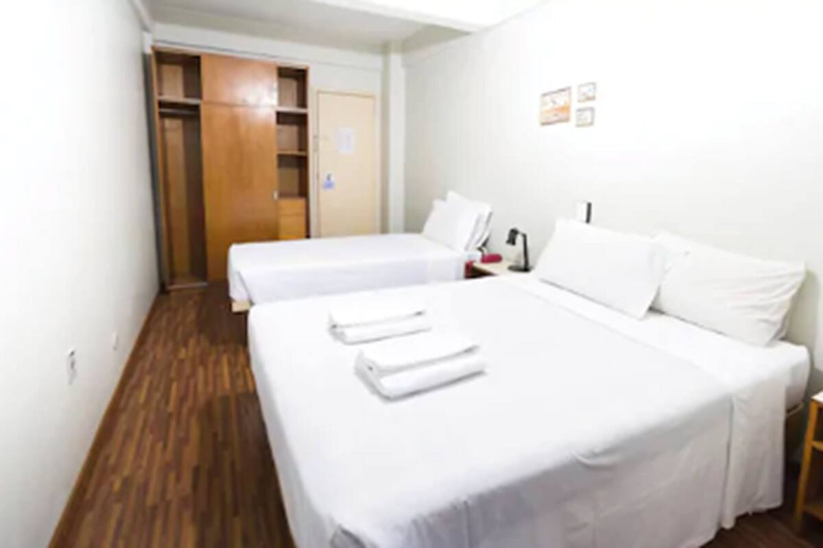 Ett hotellrum med två sängar, trägolv, vita väggar och en garderob i trä.