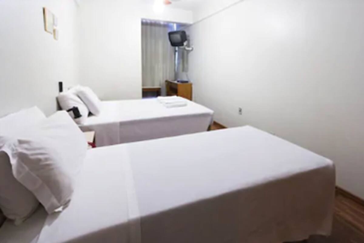 Ett hotellrum med två separata sängar, en platt-TV och ett litet bord.