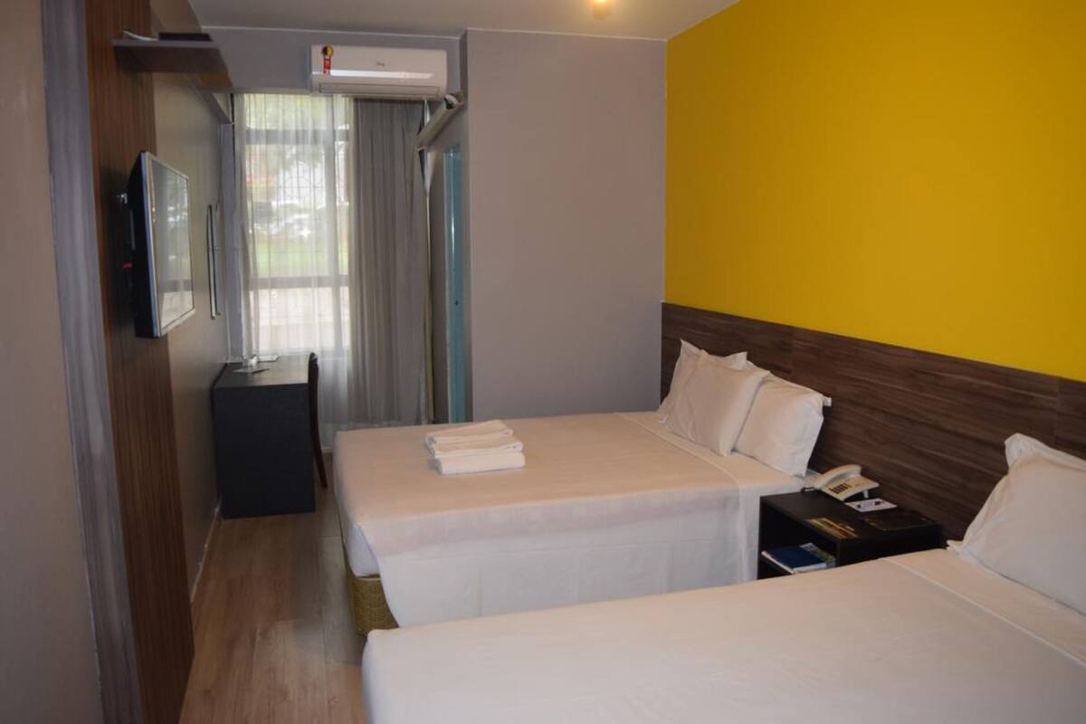 Ett hotellrum med två sängar, ett skrivbord, en TV och en luftkonditioneringsanläggning.