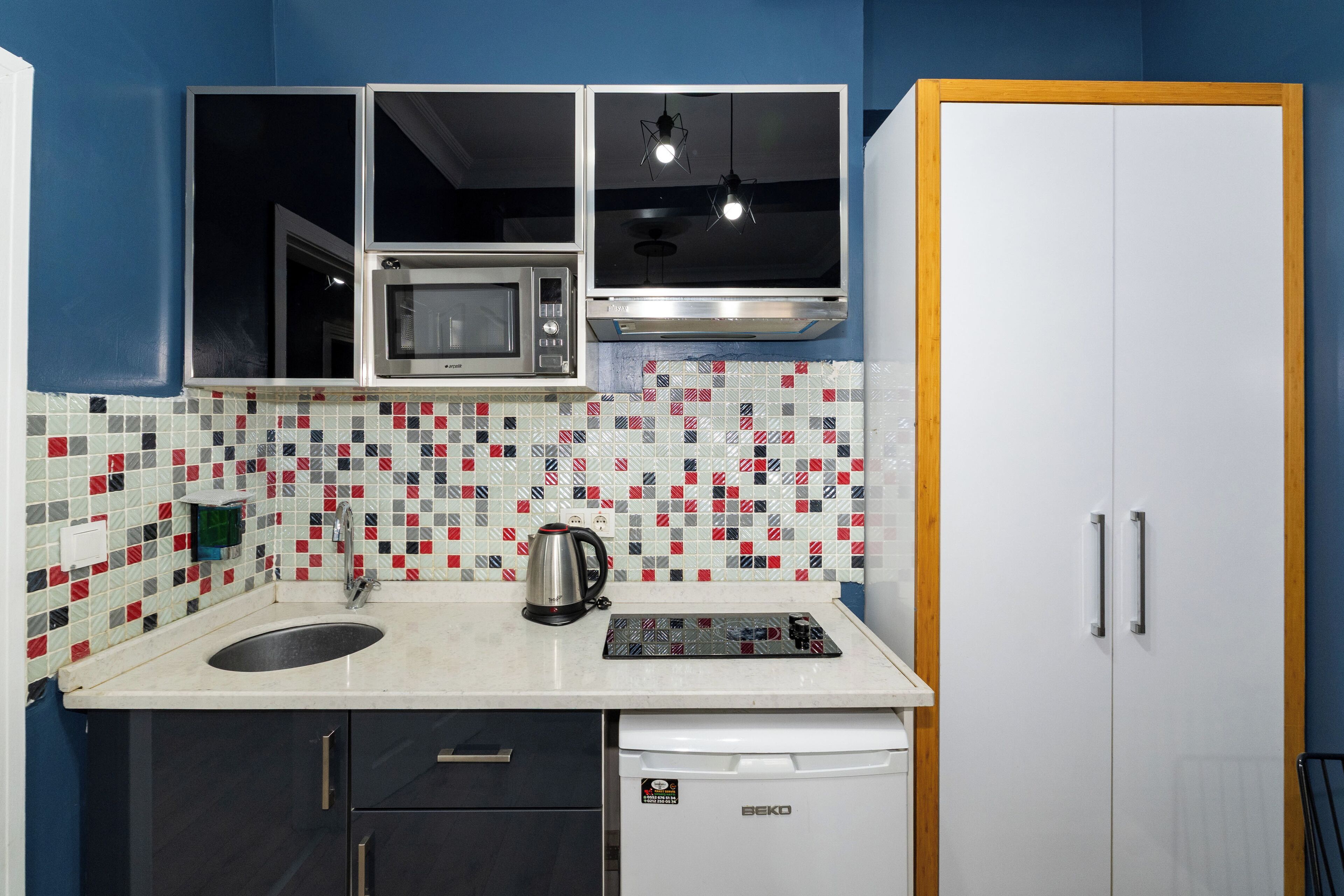 A compact kitchen with a microwave, kettle, and a coffee maker on the countertop.