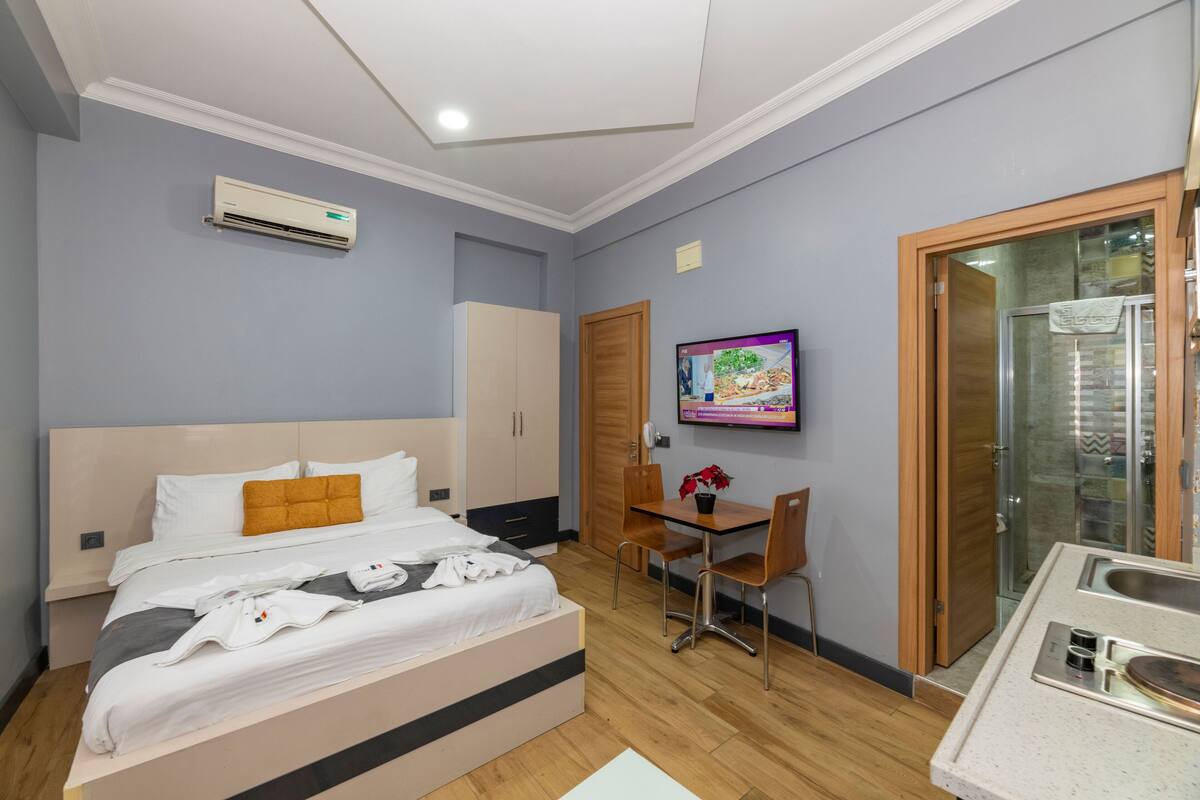 A hotel room with a bed, a desk, a chair, a TV, and a bathroom with a glass door.
