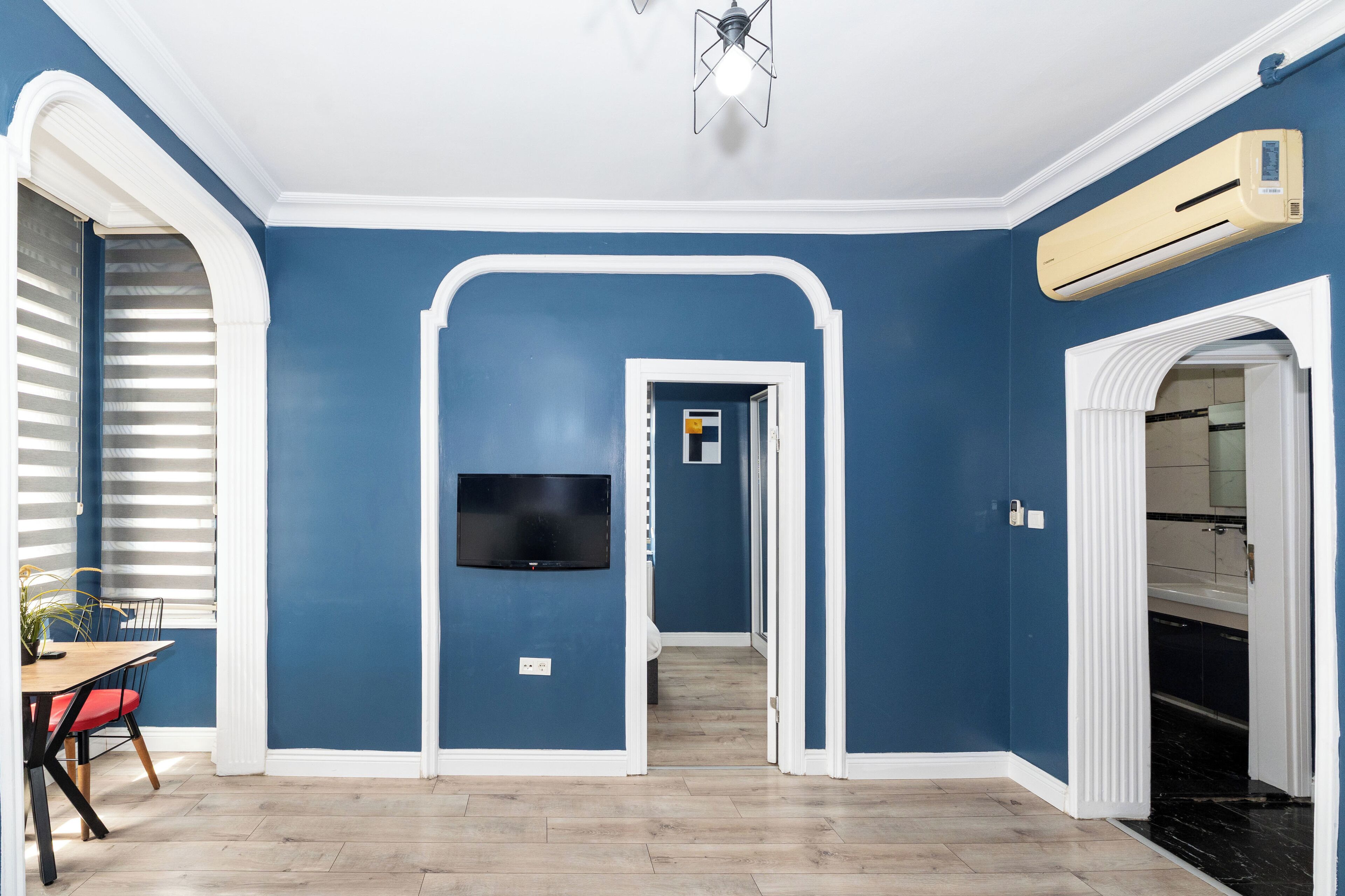 A room with blue walls, a wooden floor, a TV mounted on the wall, and an air conditioning unit.
