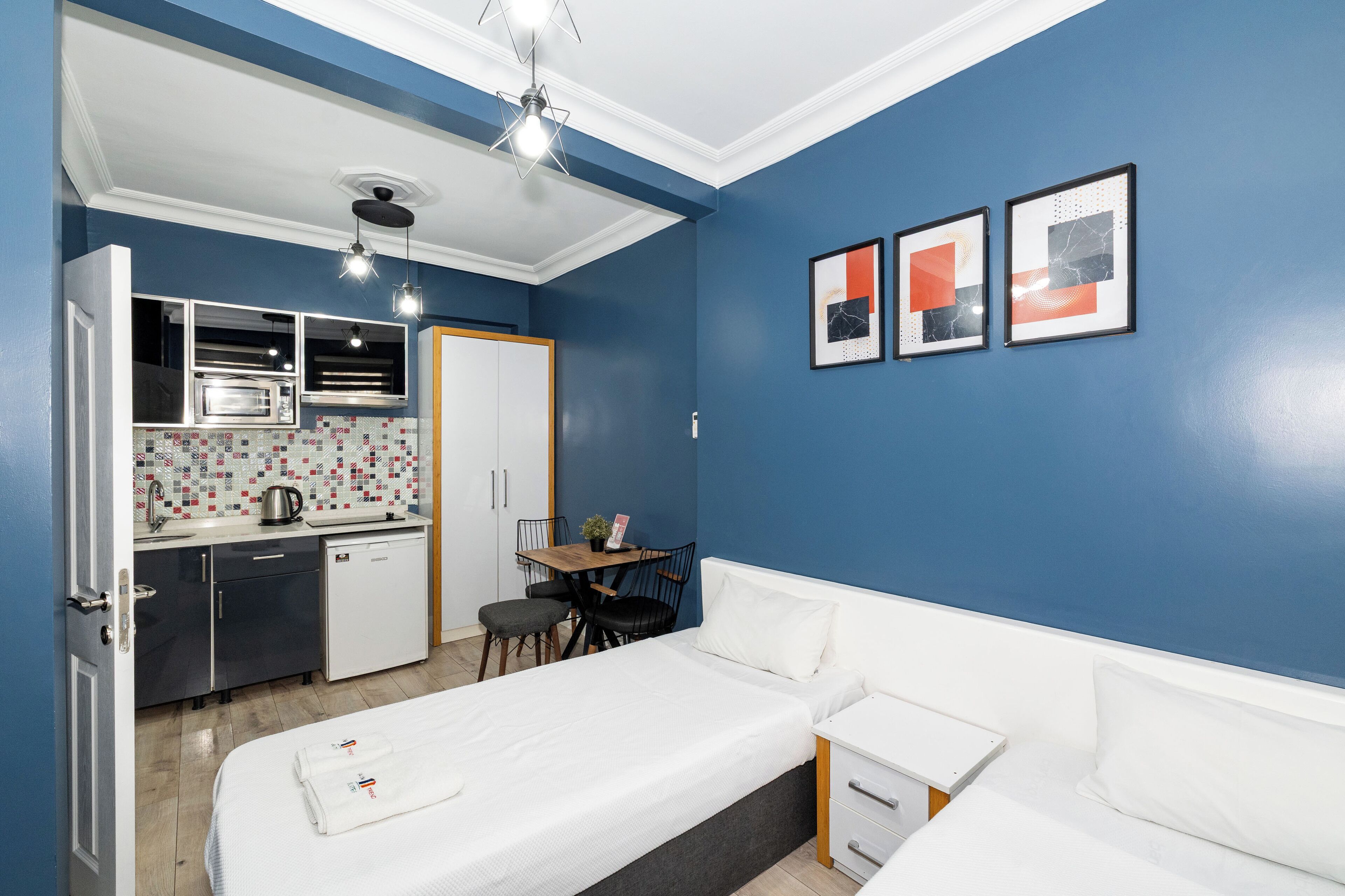 Habitació d'hotel senzilla amb cuineta, un llit, taula petita i cadires.