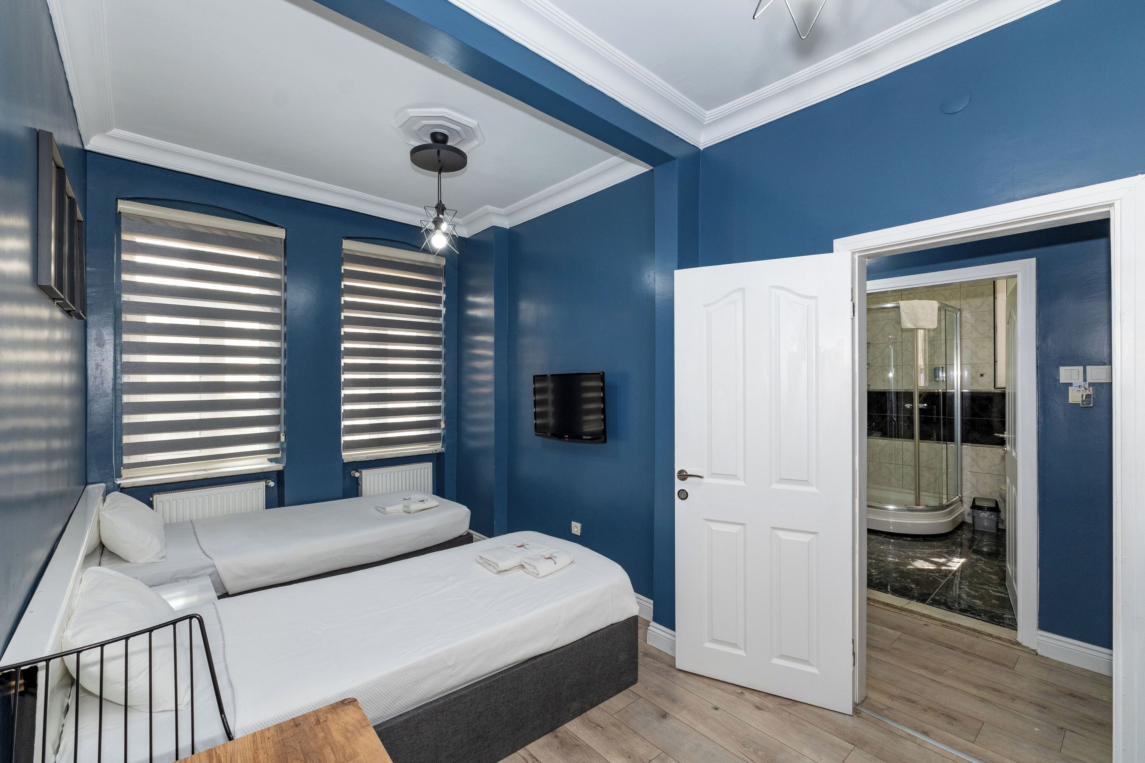 Habitación con dos camas, ventilador de techo, televisión y puerta que da a un baño con ducha.