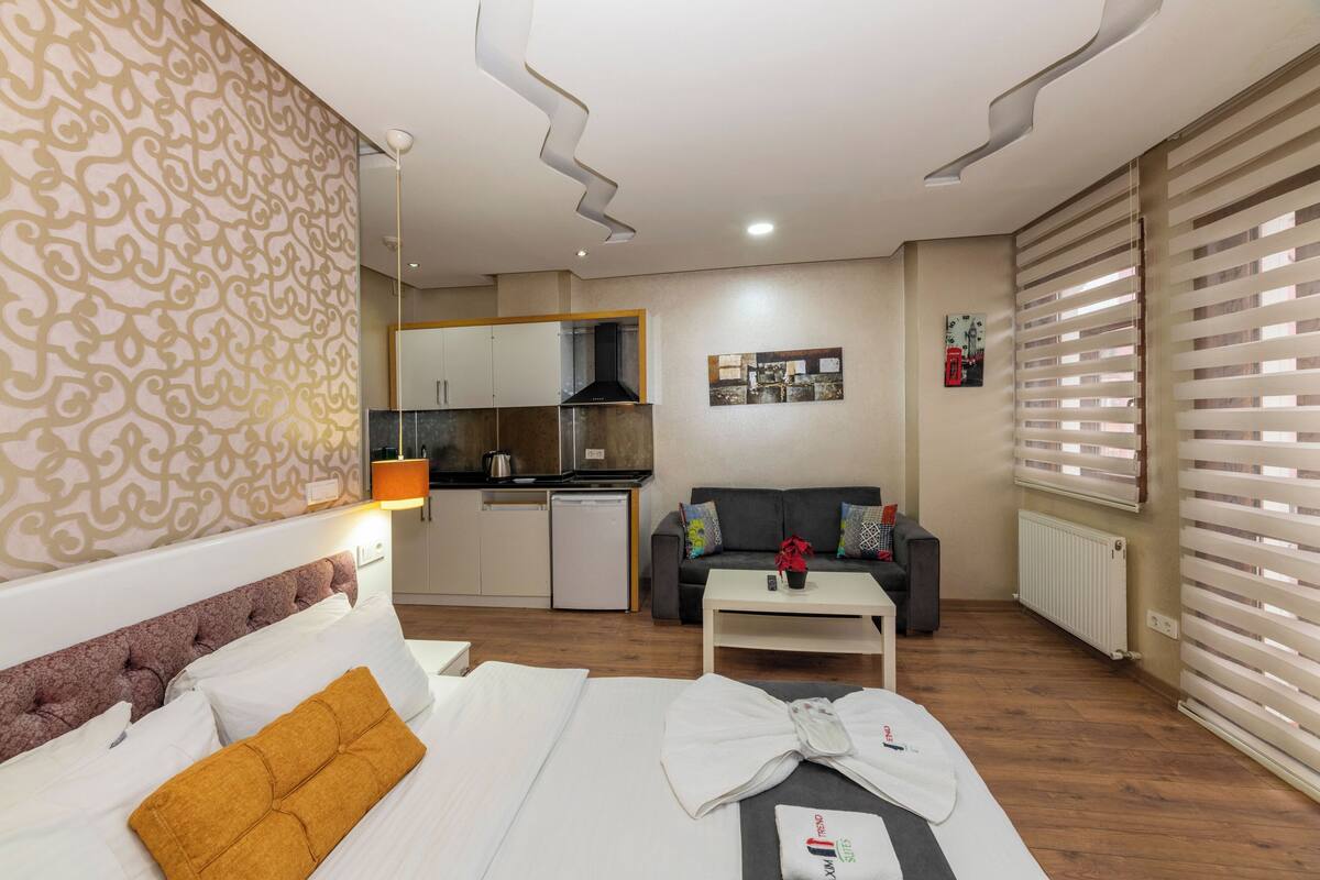 A hotel room with a bed, a sofa, a small kitchen area, and a dining table.
