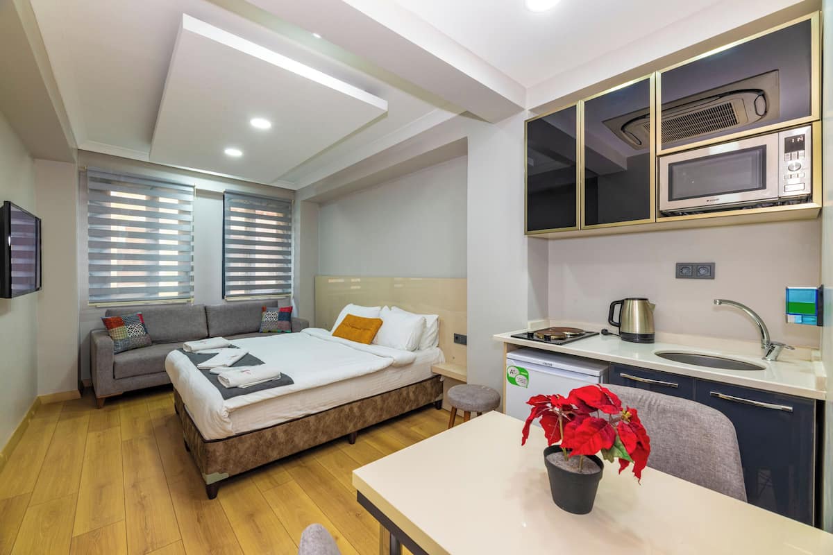 A modern hotel room with a bed, sofa, kitchenette, and a dining area.