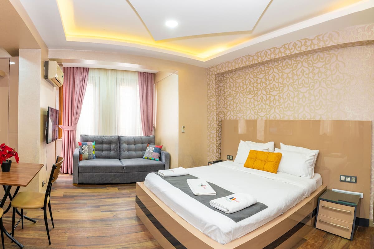 A hotel room with a bed, a sofa, a dining table with chairs, and a small table with a potted plant.