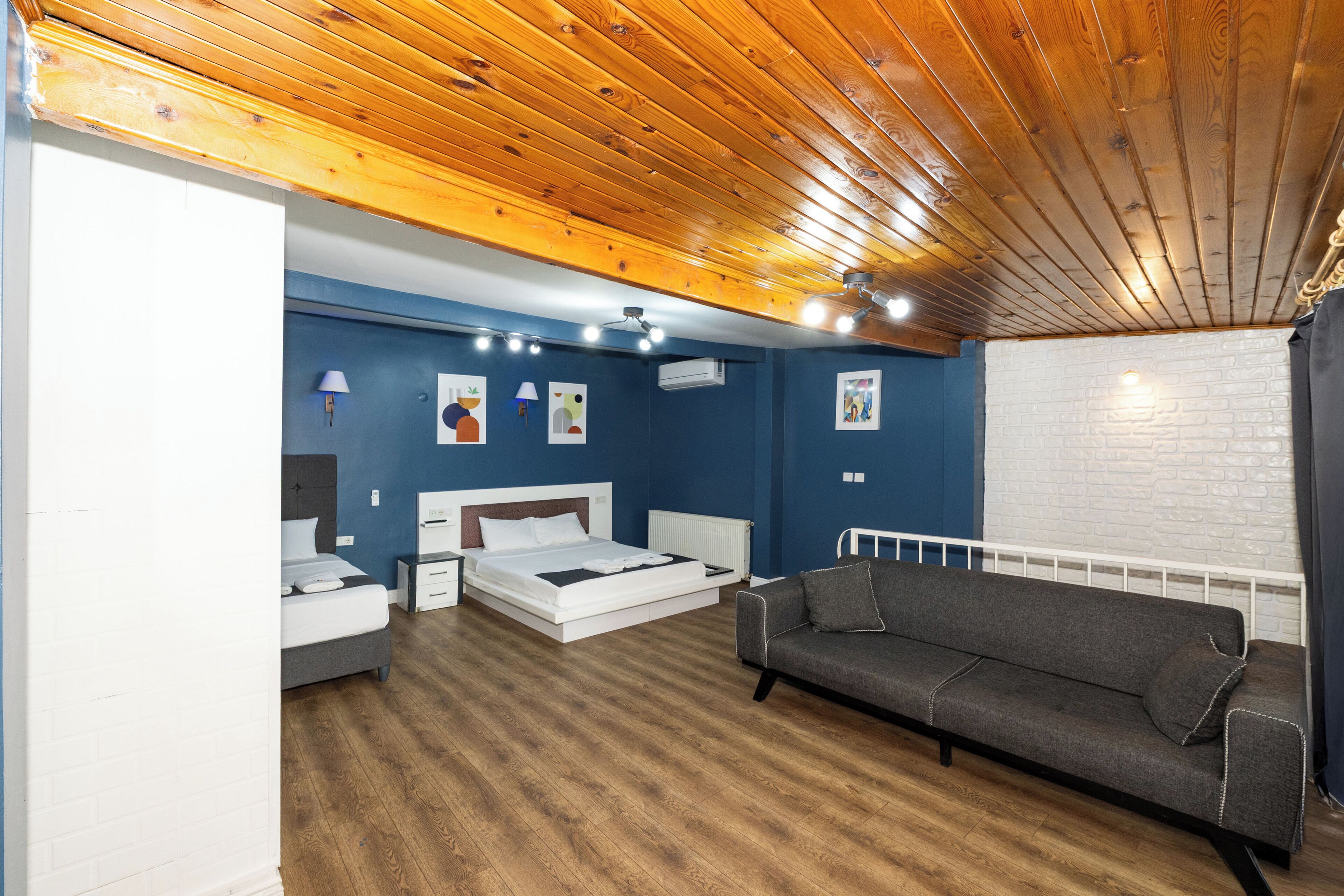Une chambre avec un plafond en bois, un lit, un canapé et un mur en briques blanches.