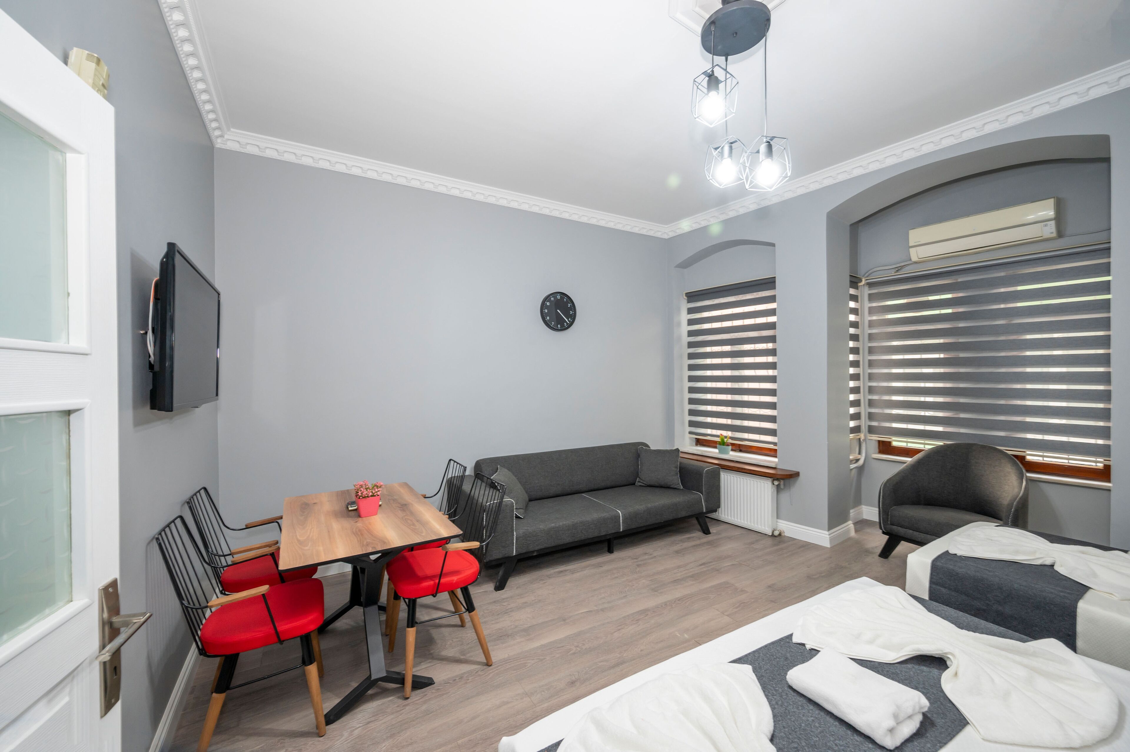 A modern room with a grey sofa, red chairs, a wooden table, and a bed with white linens.