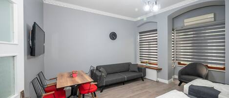 A modern room with a grey sofa, red chairs, a wooden table, and a bed with white linens.