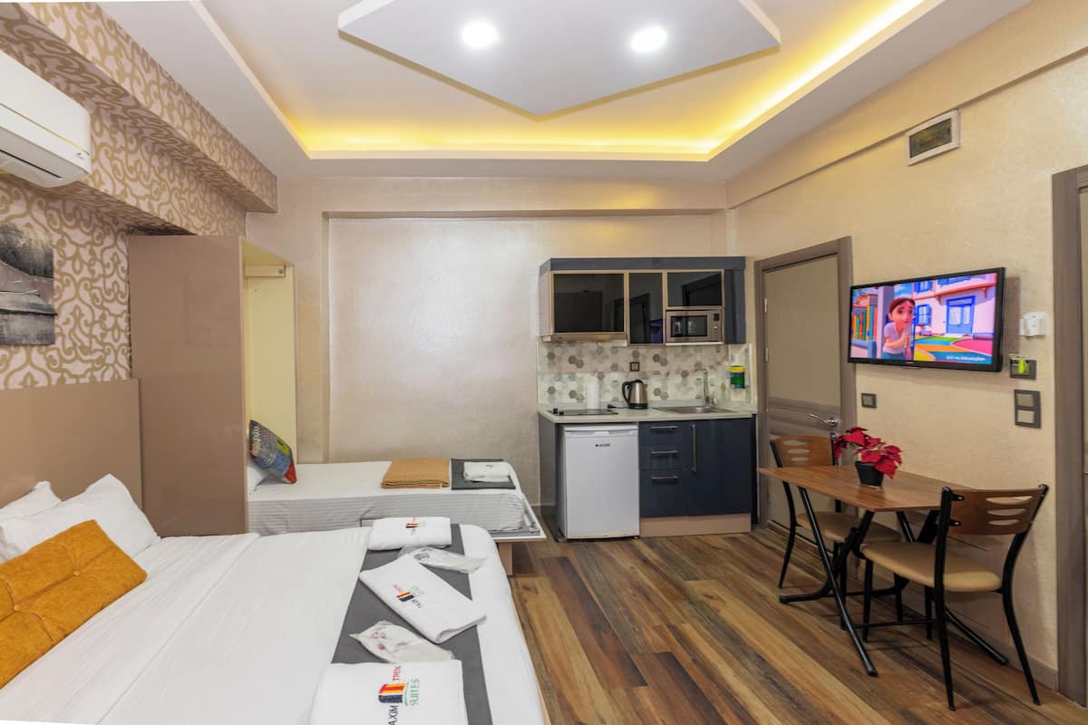A hotel room with a bed, a desk, a small kitchenette, and a TV.