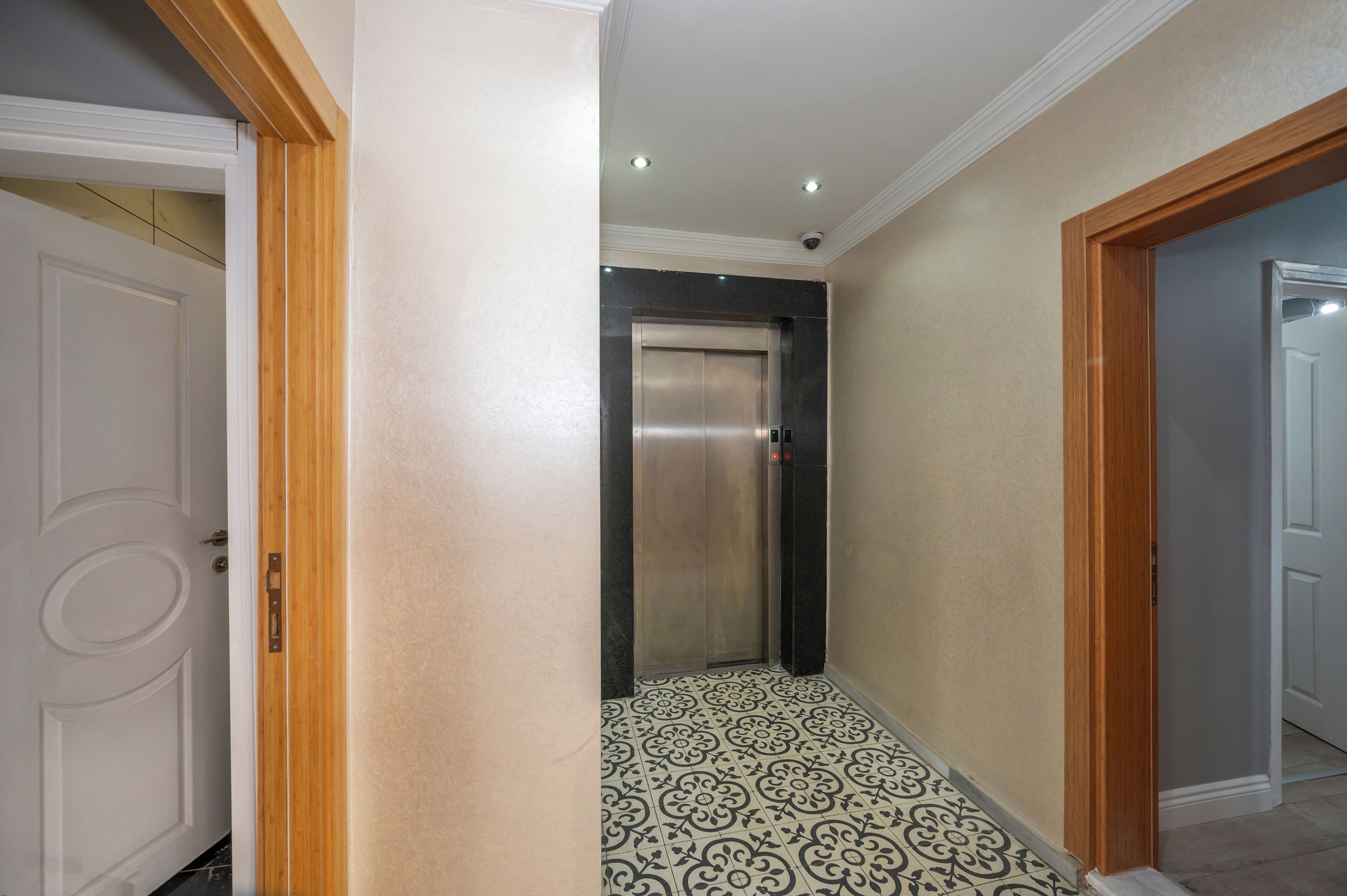 An elevator in a hallway with patterned floor tiles and wooden trim.