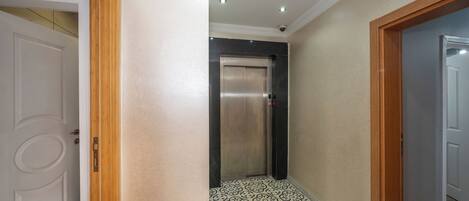 An elevator in a hallway with patterned floor tiles and wooden trim.