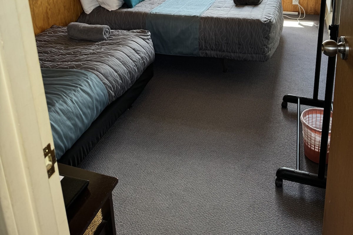 Una habitación con dos camas, vigas de madera en el techo, una ventana con cortinas y una mesita de noche con lámpara.
