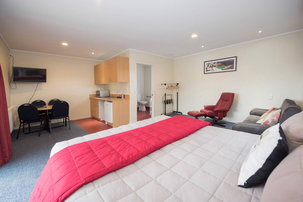 Habitación de hotel con una cama grande, un escritorio con una silla, una silla roja, un sofá y un televisor montado en la pared.