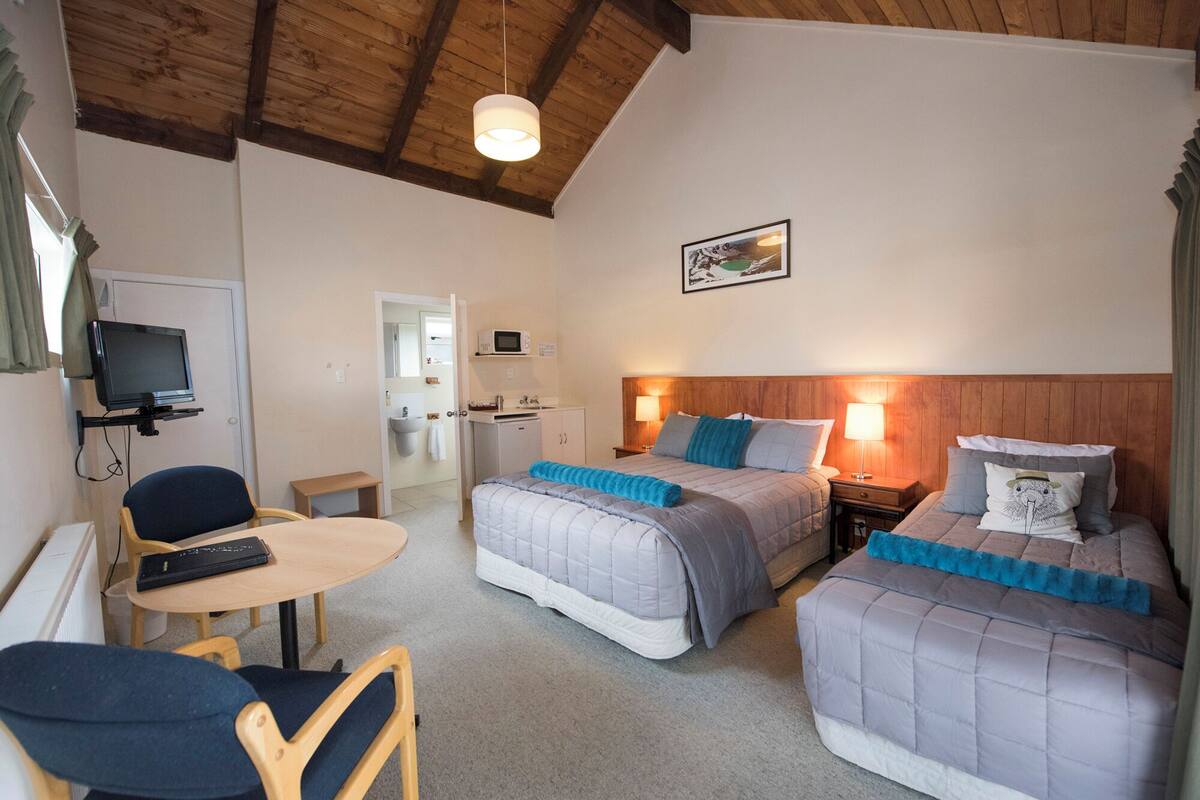 Habitación de hotel con dos camas, un escritorio con silla, televisor y baño visible a través de una puerta abierta.
