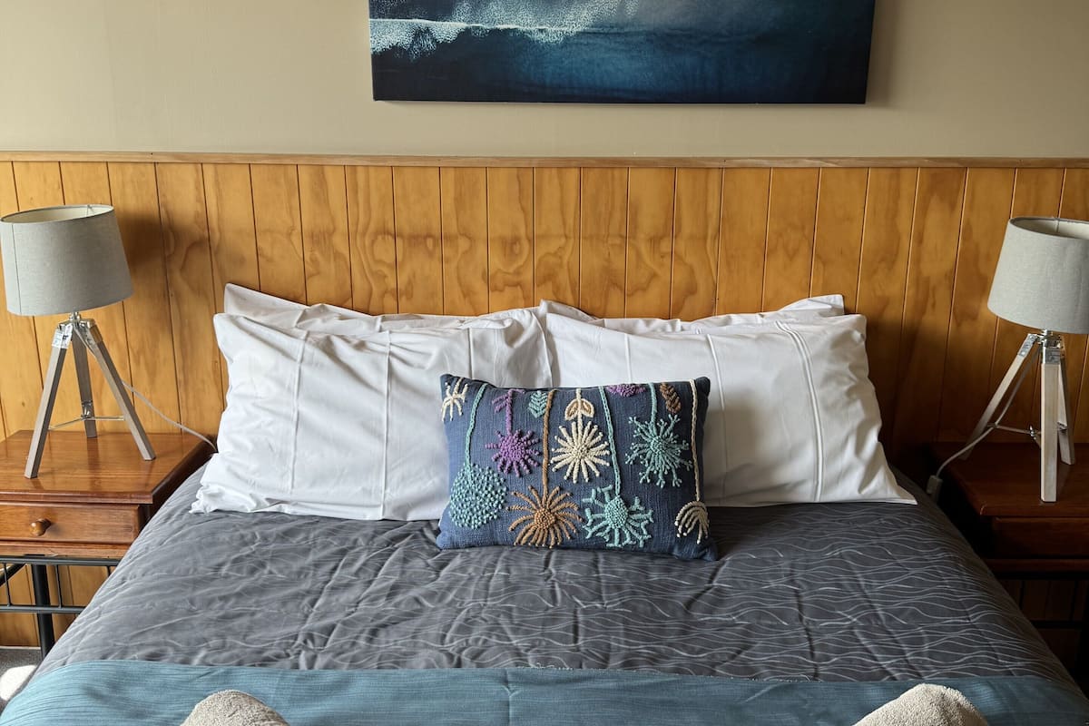 Una cama bien hecha con una colcha azul, dos toallas enrolladas y una almohada decorativa.