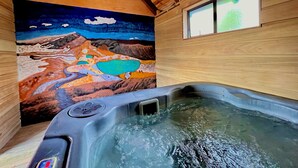 A wooden cabin interior with a hot tub and a mural of a mountainous landscape.