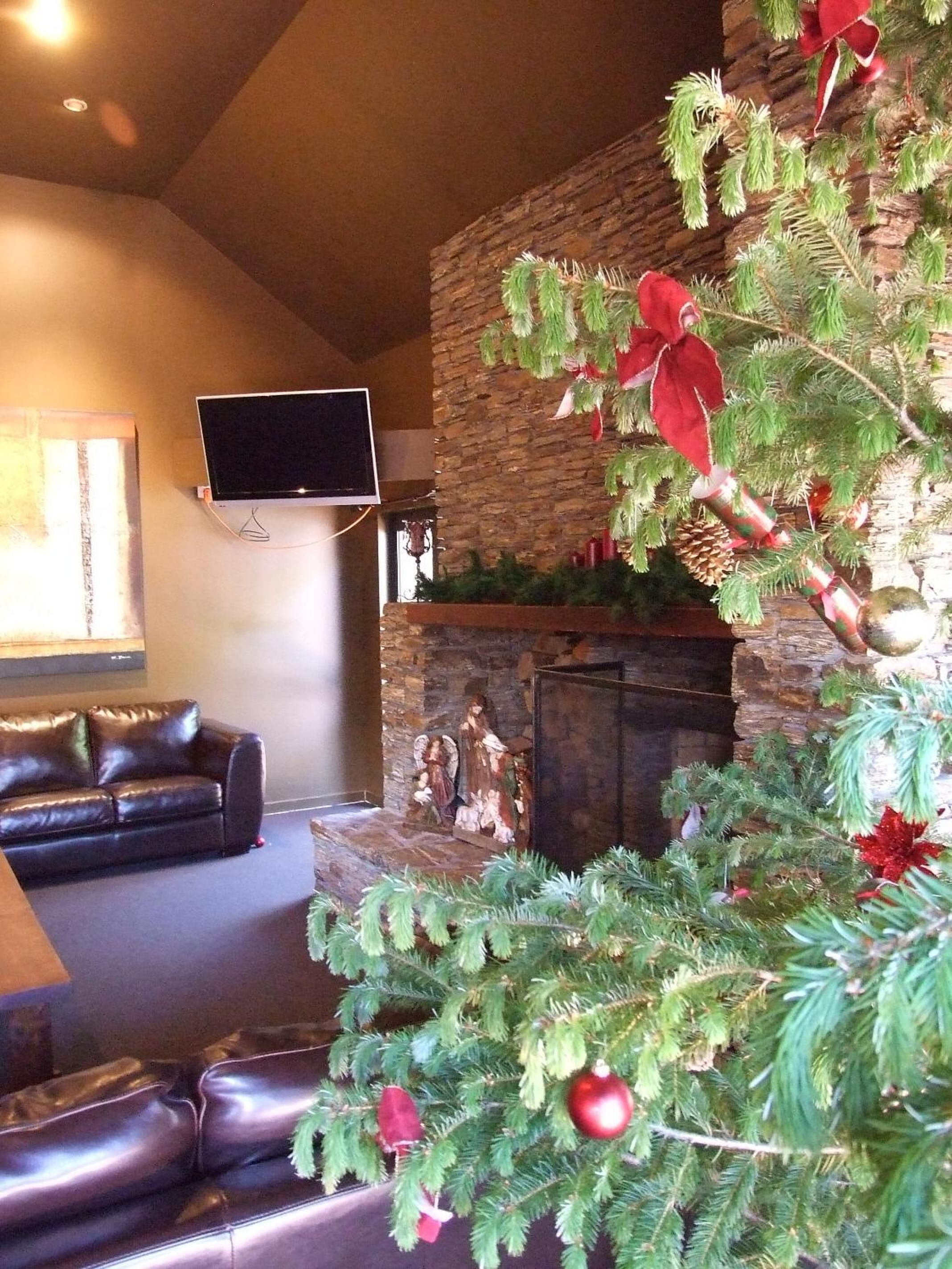 A living room with a fireplace, a stone wall, a flat-screen TV mounted above the fireplace, and a leather sofa.