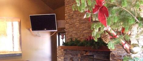 A living room with a fireplace, a stone wall, a flat-screen TV mounted above the fireplace, and a leather sofa.