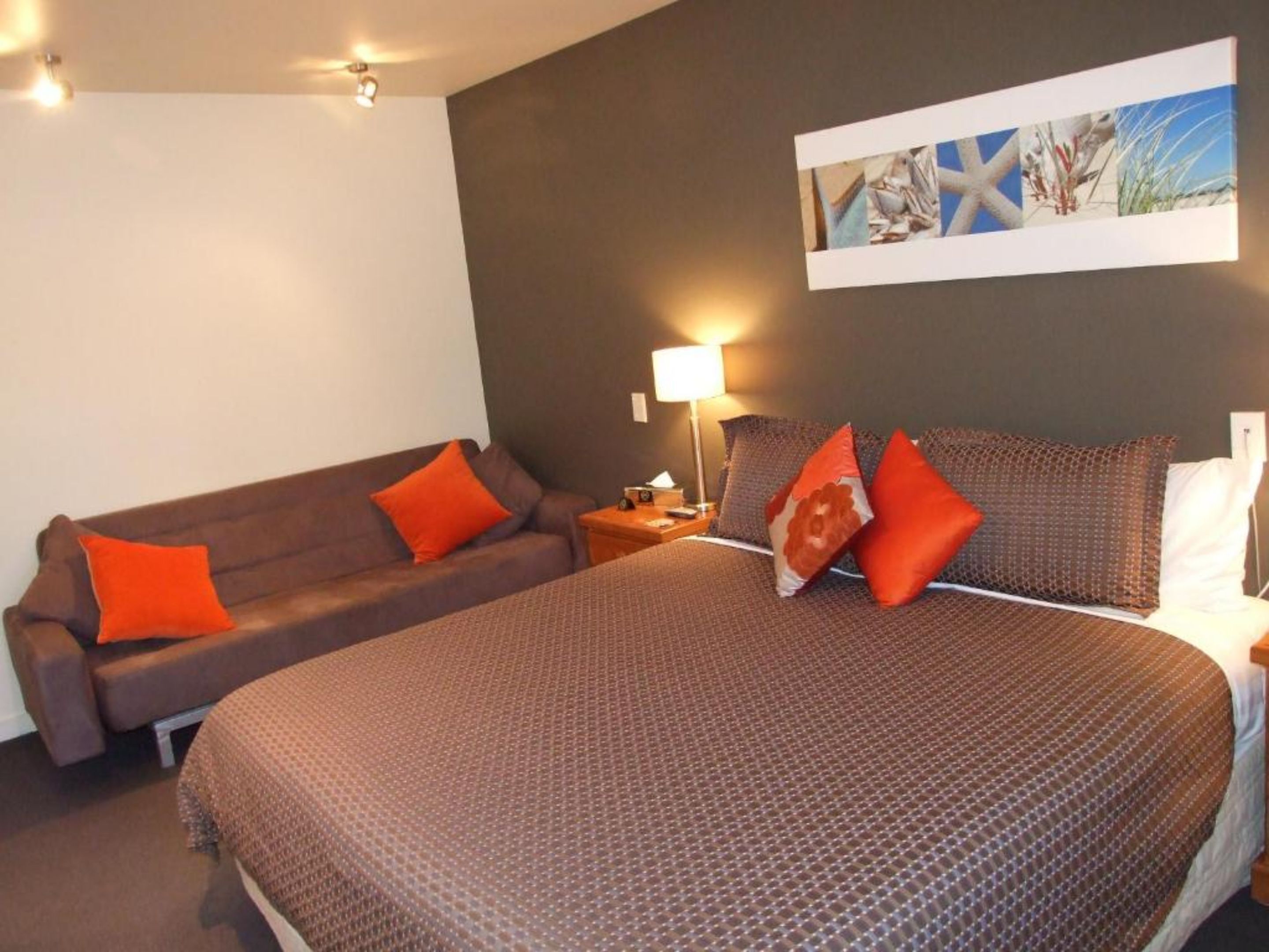 A hotel room with a large bed, a brown sofa, and a wall-mounted artwork.