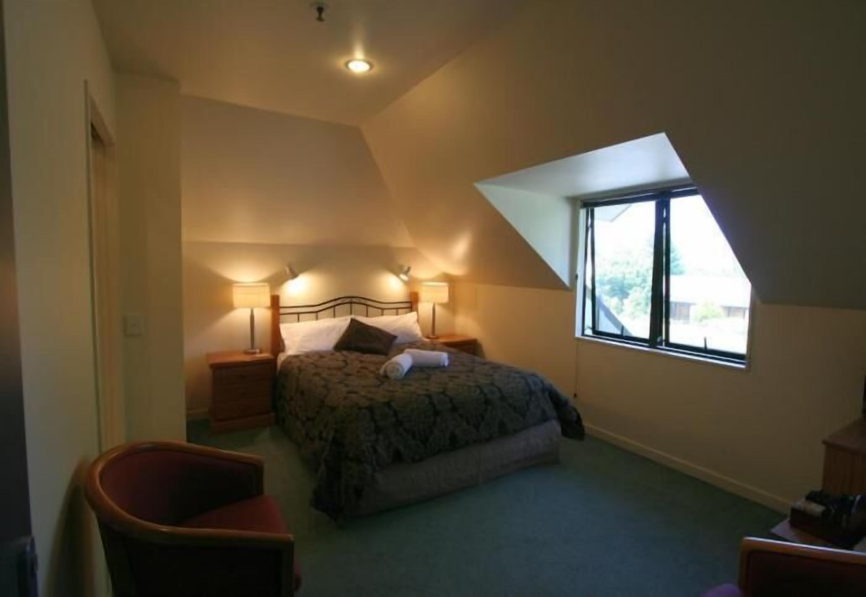 Un dormitorio con una cama, dos mesitas de noche, una silla y una ventana.