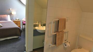 Habitación de hotel con cama, mesita de noche con lámpara, baño con lavabo, espejo y retrete.