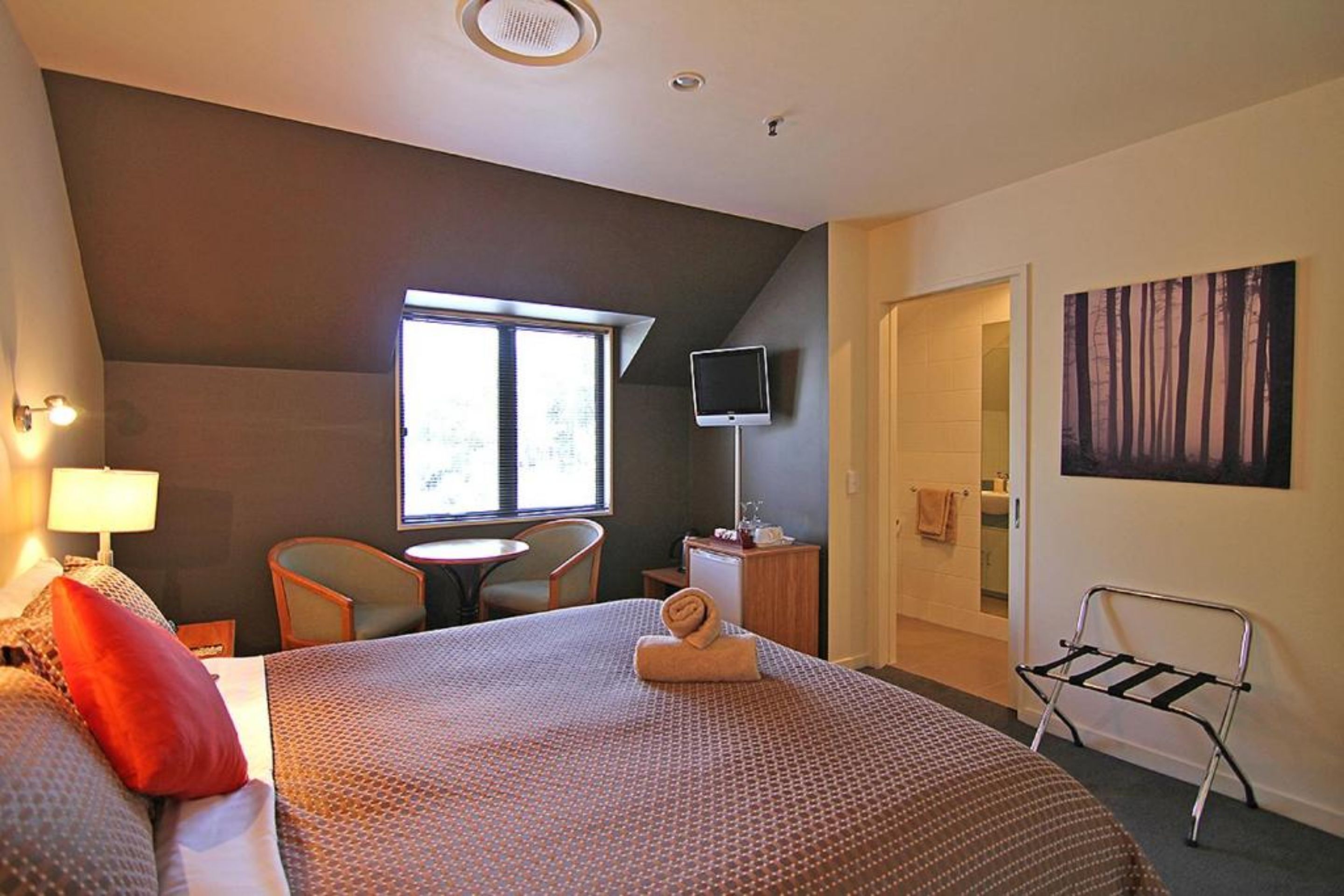 A hotel room with a large bed, a desk, a chair, a TV, and a window.