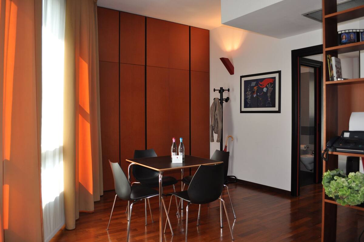 A modern room with a wooden floor, a dining table with chairs, a bookshelf, and a framed picture on the wall.